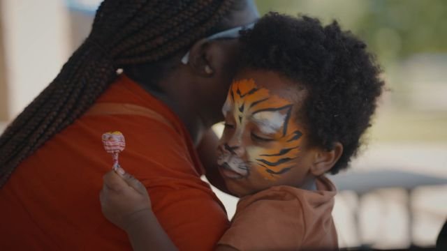 A boy with a tiger face painting hugging his mom