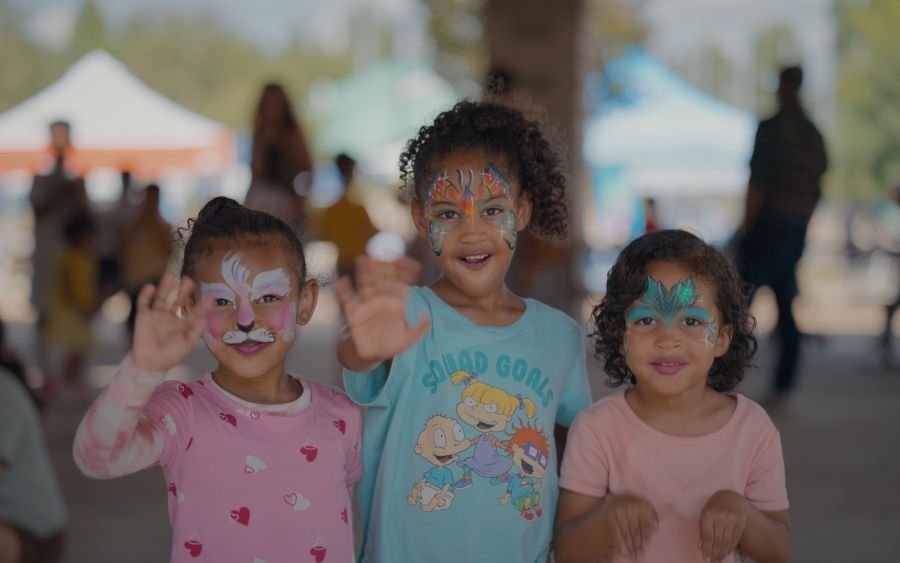 Three face-painted kids waving at an outdoor festival in Metro Atlanta