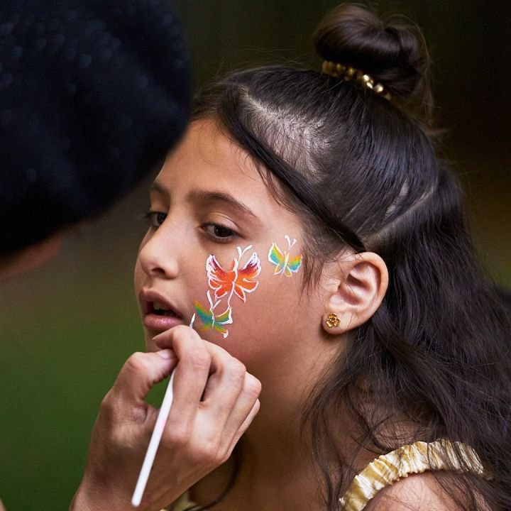 A girl getting a rainbow butterfly painted on her cheek