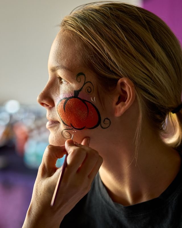 A girl in profile with a glowing orange pumpkin painted on her cheek