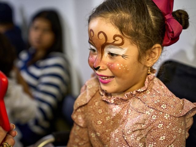 A smiling girl with a reindeer face painting and a big red bow