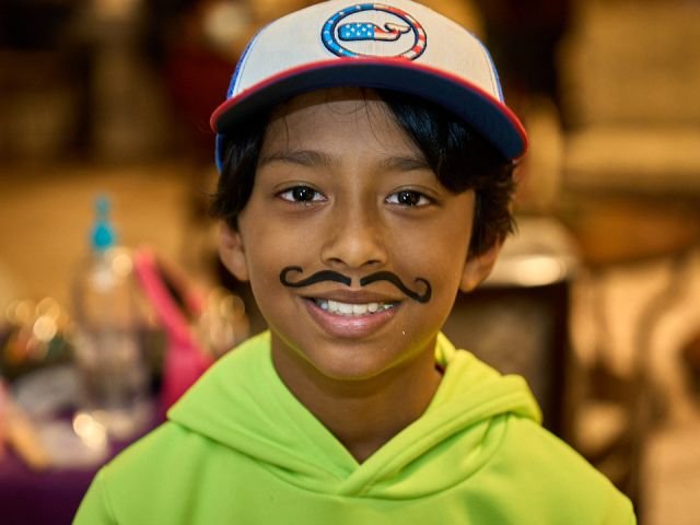 A boy in a cap grinning with a painted mustache