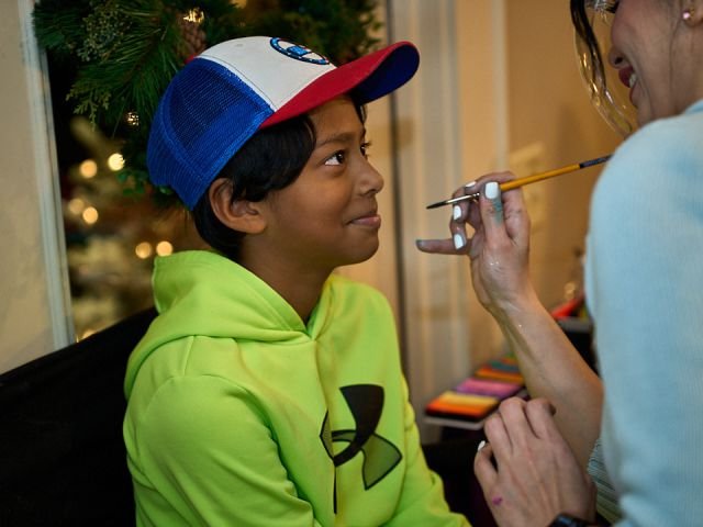 A face painter carefully painting a boy’s face at a holiday party