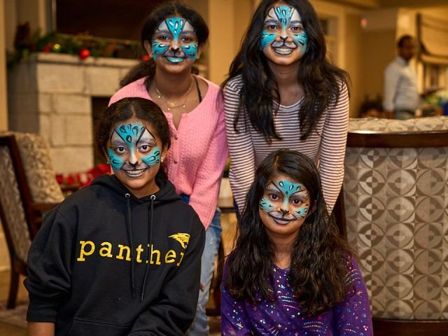 Four friends showing off matching blue cat face paintings