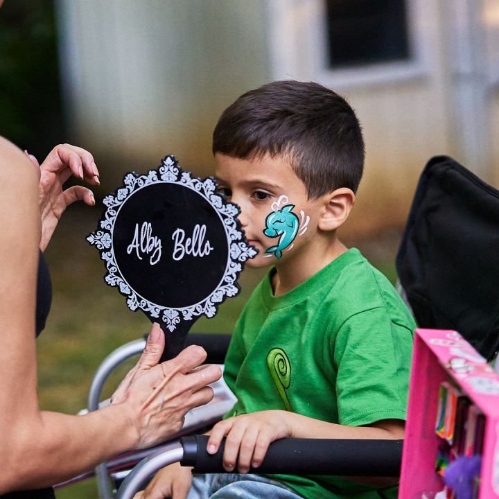 A boy admiring the dolphin painted on his cheek in an Alby Bello mirror