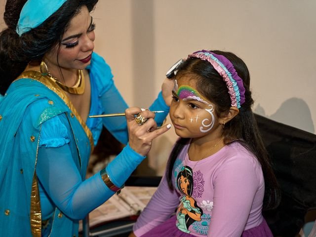 Princess Jasmine painting a rainbow design on a young fan