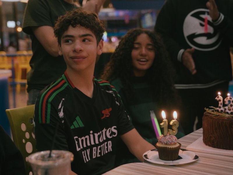 A birthday boy smiling beside his candle-lit cake at a bowling alley party