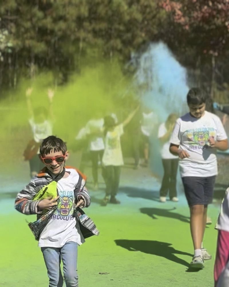 A boy in sunglasses racing through clouds of green color at a school color run
