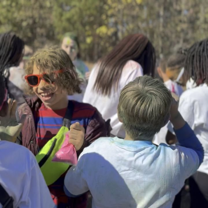 A smiling kid in orange sunglasses surrounded by friends at a color run