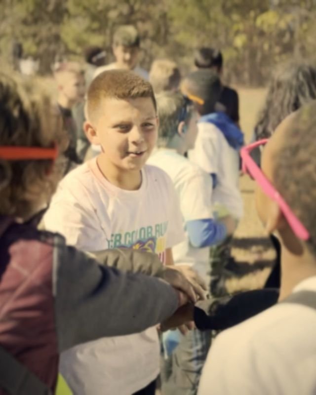Kids in colorful sunglasses grinning together at a school color run
