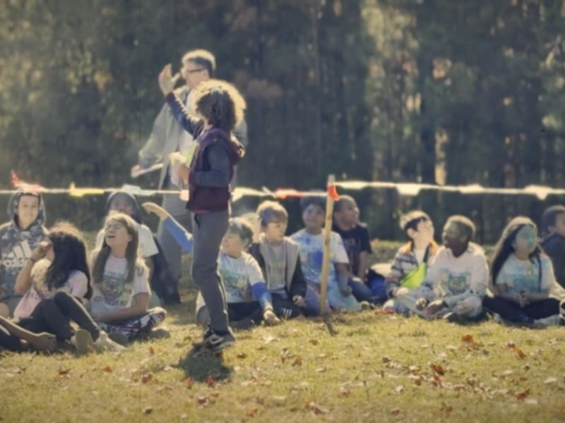 A game leader cheering on rows of seated students at a school color run