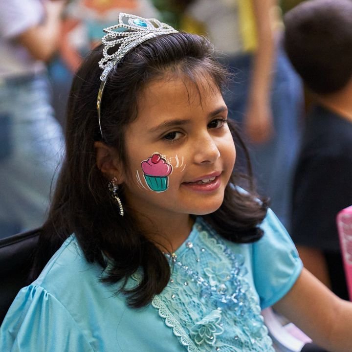 A birthday girl in a tiara with a cupcake painted on her cheek