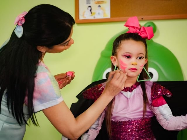 A face painter adding sparkle to a birthday girl in a pink sequin dress