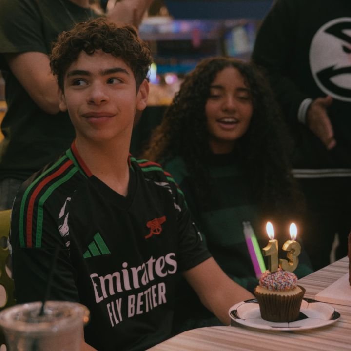A birthday boy smiling beside his candle-lit cupcake